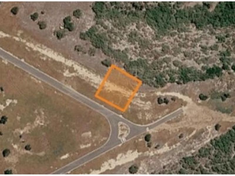 An aerial view of a vacant residential plot highlighted in orange, situated near an access road and natural vegetation.