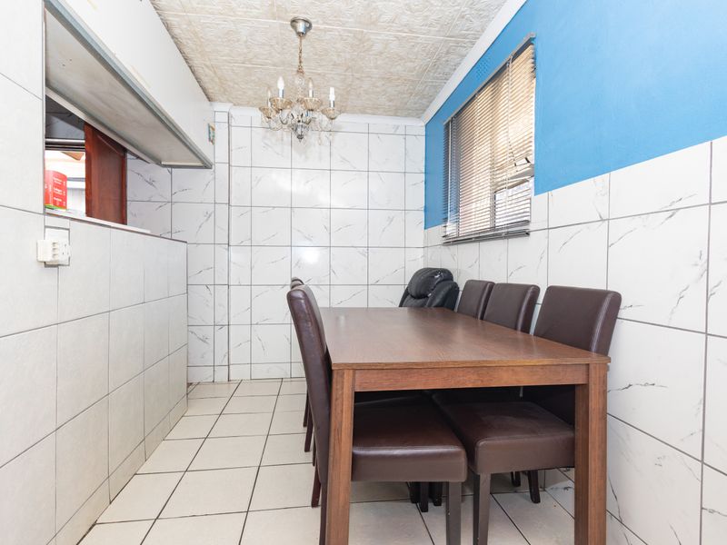 Dining area featuring tiled walls and flooring, a decorative ceiling, and a convenient serving hatch connecting to the kitchen space.