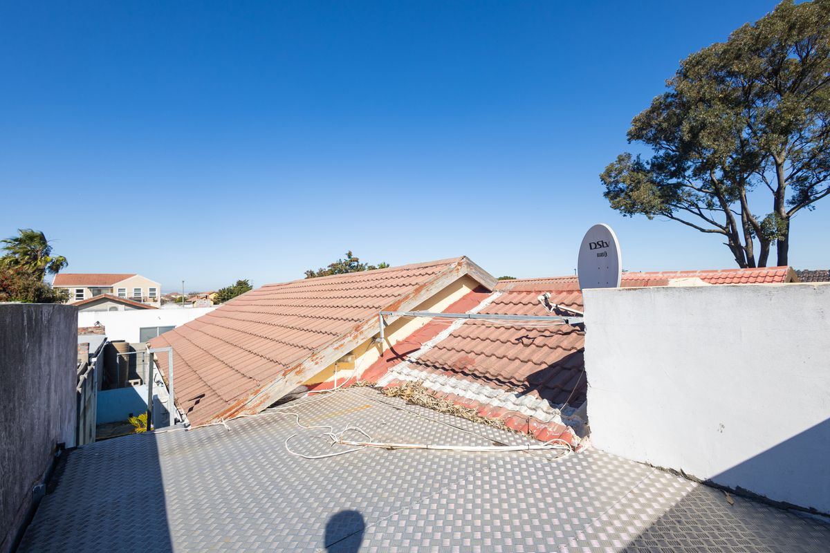 An elevated view of the property roof structure featuring tiled roofing, a satellite dish, and a metal deck area with visible maintenance requirements.