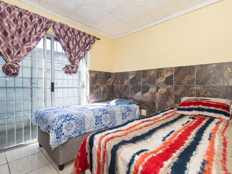 A bedroom featuring tiled flooring, tiled wall accents, and a sliding glass door with security gate access to the exterior.