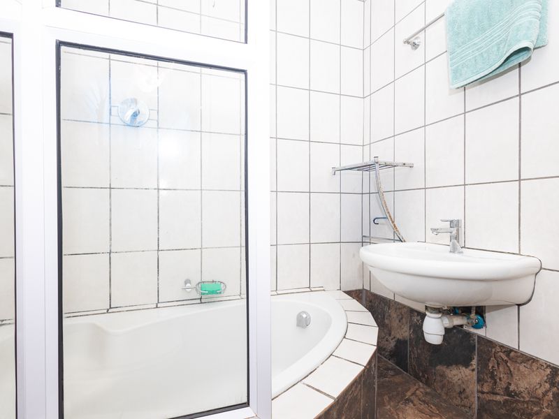 A compact bathroom featuring a built-in bathtub, shower enclosure, and wall-mounted basin with tiled finishes throughout.