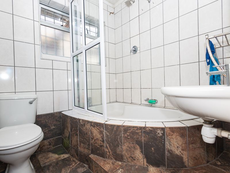 A functional bathroom featuring a built-in bathtub with a shower screen, pedestal washbasin, and toilet, finished with tiled walls and flooring.