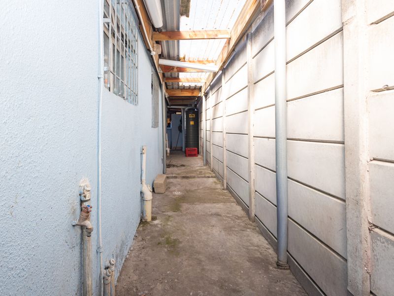 A narrow utility side passage featuring a concrete boundary wall, translucent roof covering, and external plumbing fixtures.