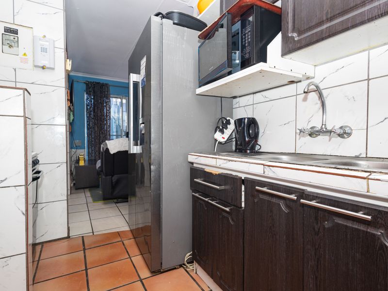 Compact kitchen featuring dark wood cabinetry, tiled backsplash, and a double sink, showing signs of wear and requiring cosmetic updates.