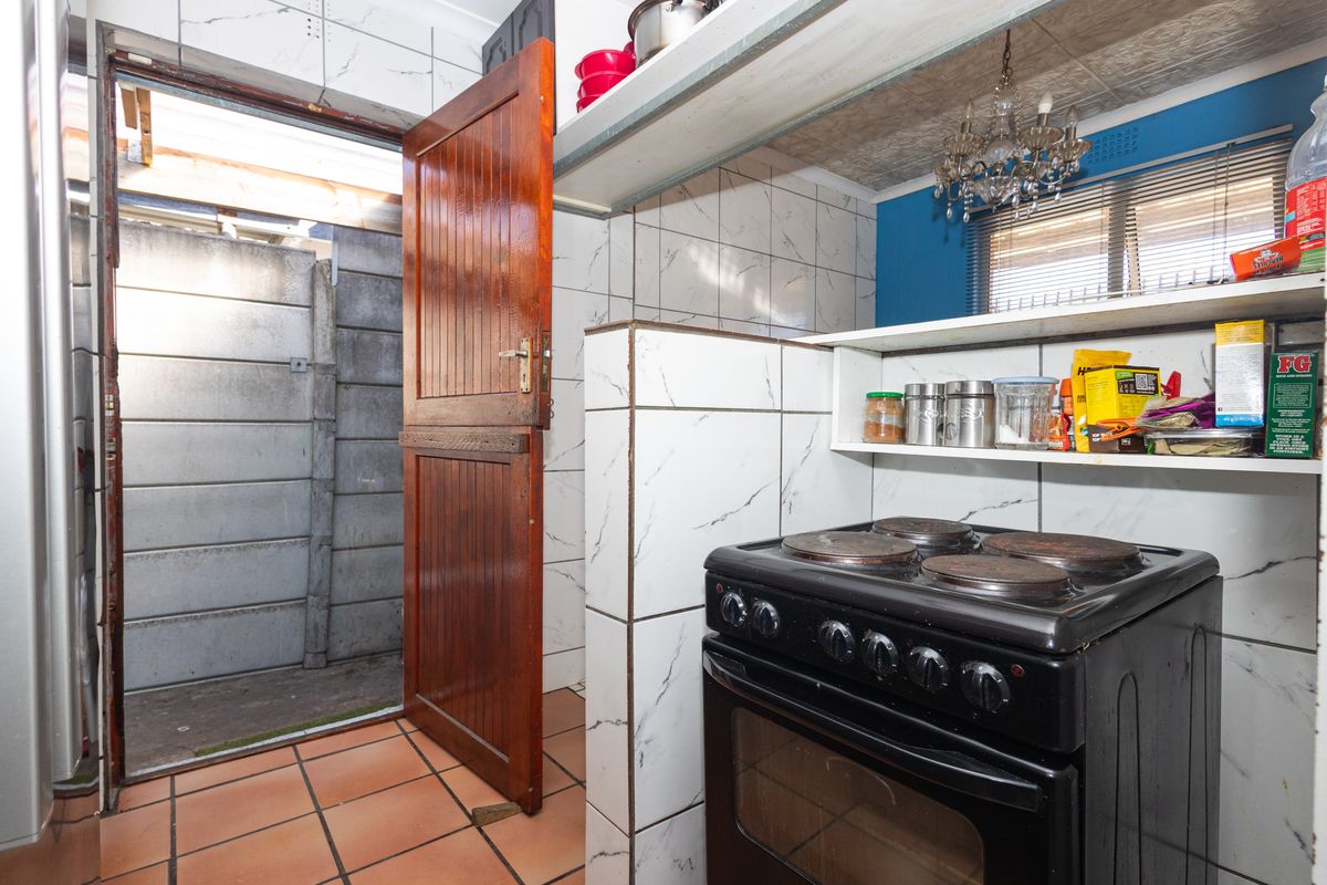 A compact kitchen area featuring tiled walls, built-in shelving, and a freestanding electric stove, with direct access to an outdoor utility space.