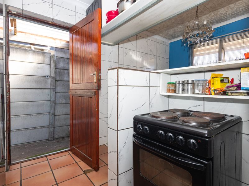 A compact kitchen area featuring tiled walls, built-in shelving, and a freestanding electric stove, with direct access to an outdoor utility space.