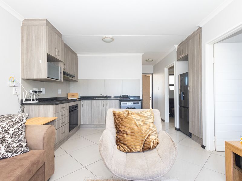 Open-plan kitchen featuring modern wood-grain cabinetry, laminate countertops, built-in oven, and tiled flooring, seamlessly integrated into the living area.