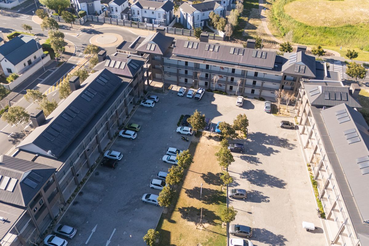 Aerial view of the apartment complex showing the building layout, pitched metal roofs with skylights, and the central paved parking area.