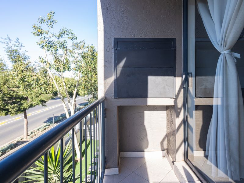 A private balcony featuring a built-in braai, tiled flooring, and a metal railing, offering an outdoor space accessible via sliding glass doors.