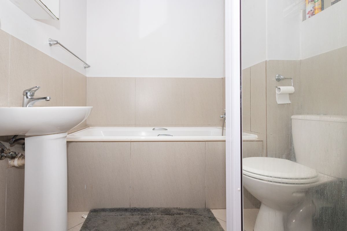 A functional bathroom featuring a pedestal basin, built-in bathtub, and toilet with neutral wall tiling.