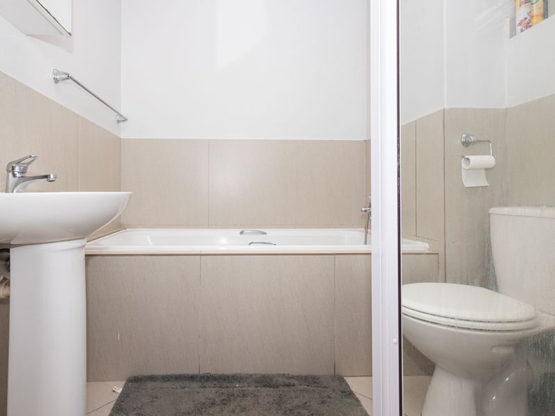 A functional bathroom featuring a pedestal basin, built-in bathtub, and toilet with neutral wall tiling.
