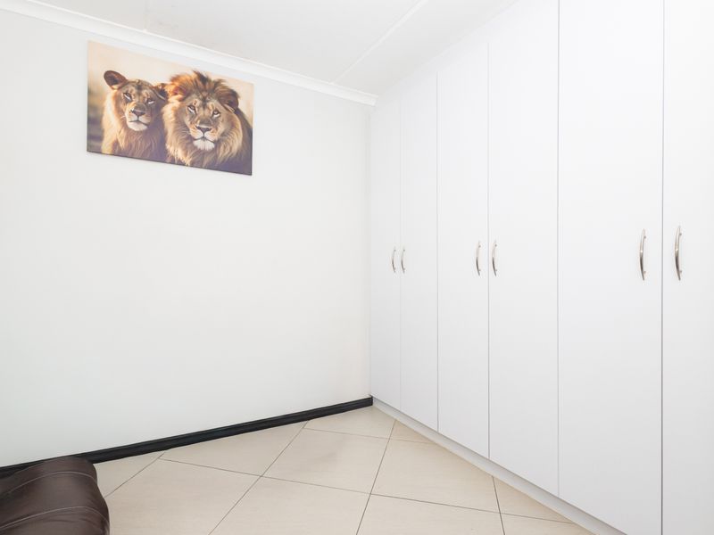 A clean bedroom featuring neutral tiled flooring and extensive white built-in cupboards providing ample storage space.