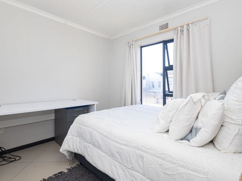 A bright bedroom featuring tiled flooring, neutral walls, and an aluminium-framed window, providing a clean and functional living space.