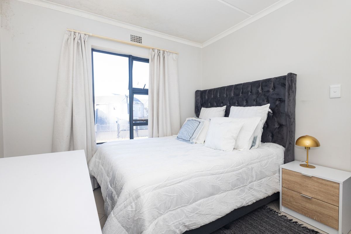 A well-lit bedroom featuring a large window with aluminium frames and neutral wall finishes.