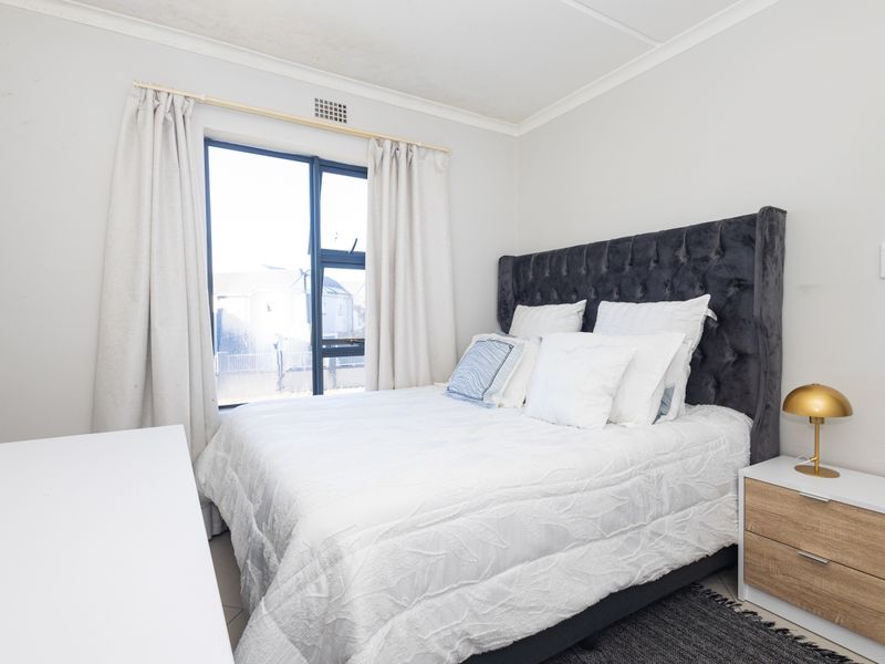A well-lit bedroom featuring a large window with aluminium frames and neutral wall finishes.