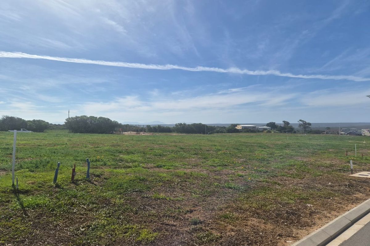 A vacant residential plot of land featuring natural grass cover, visible utility connection points, and a concrete curb along the street frontage.