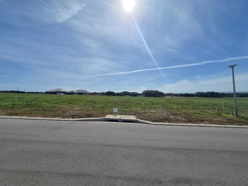 A view of a vacant residential plot featuring a paved road, concrete curb, stormwater drainage, and a street light.