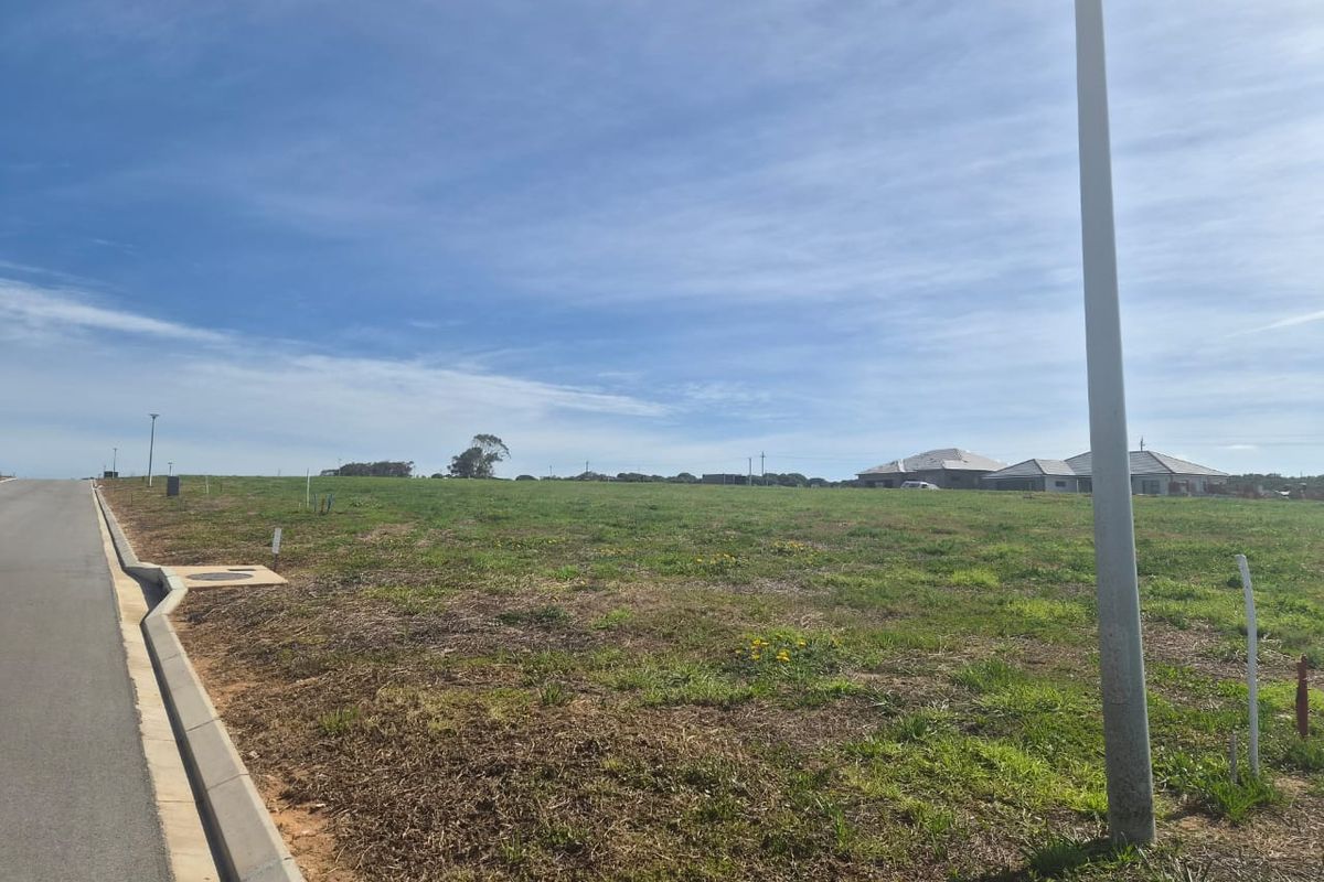 A vacant residential land parcel featuring a level grassed surface, adjacent to a paved road with established curb and utility infrastructure.
