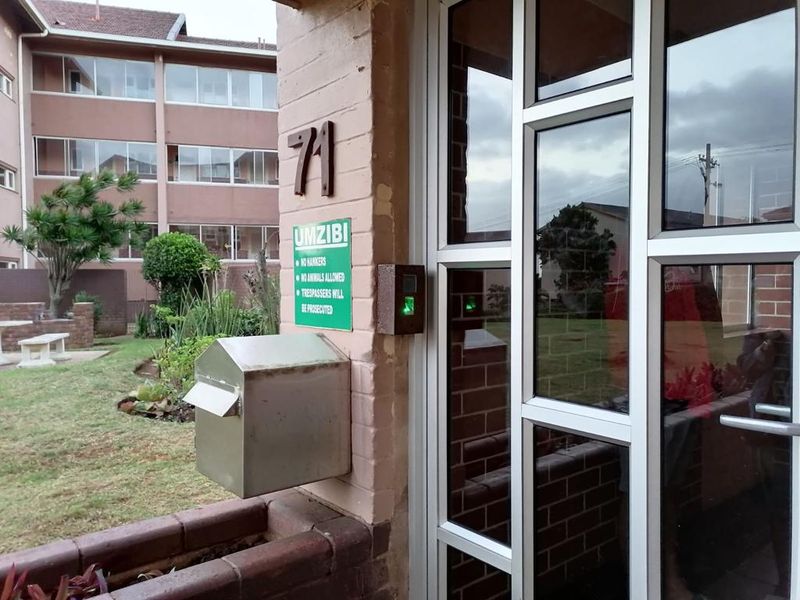 Entrance area of the Umzibi building featuring an aluminium framed glass door, secure intercom system, and a stainless steel mailbox.