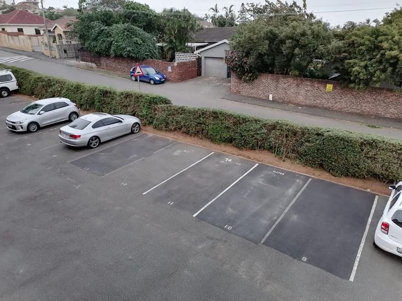 An elevated view of an asphalt parking area with marked bays, adjacent to a residential street with brick boundary walls and established greenery.