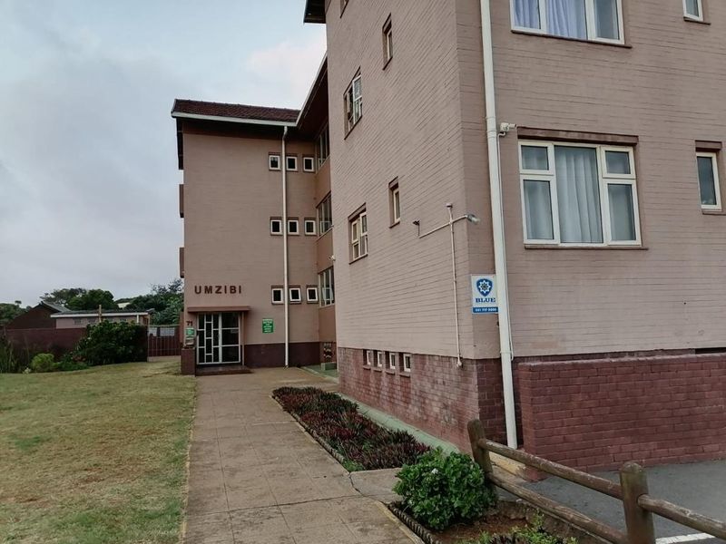 Exterior view of the Umzibi apartment building featuring a brick facade, paved entrance walkway, and established communal garden area.