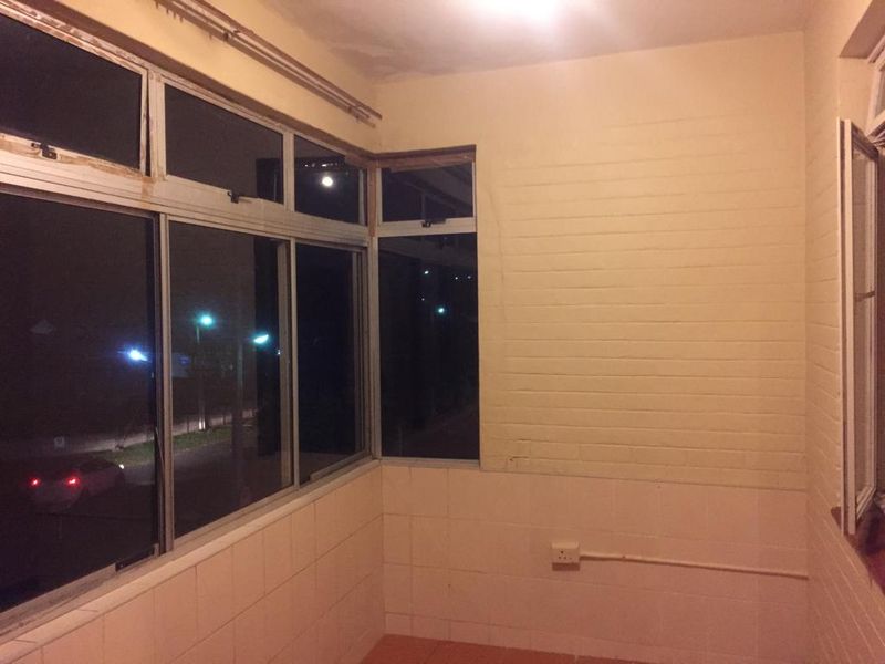 An enclosed balcony or sunroom featuring tiled walls, aluminium window frames, and tiled flooring, currently in need of cosmetic refurbishment.