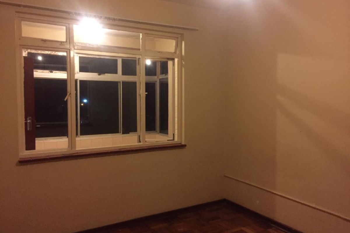 An empty bedroom featuring original parquet flooring and large metal-framed windows, offering a blank canvas for renovation.