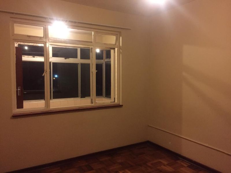 An empty bedroom featuring original parquet flooring and large metal-framed windows, offering a blank canvas for renovation.