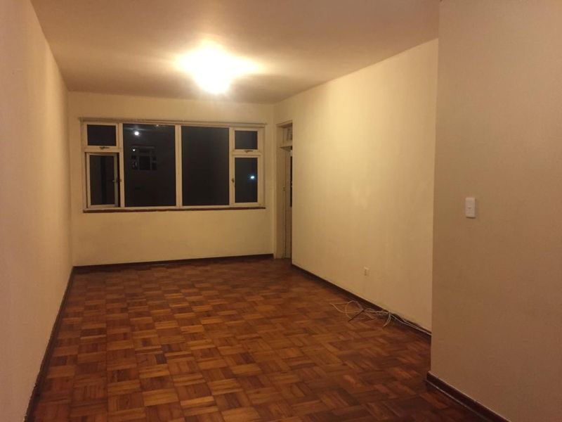 An empty living room featuring original parquet flooring and large windows, offering a blank canvas for renovation and interior design.