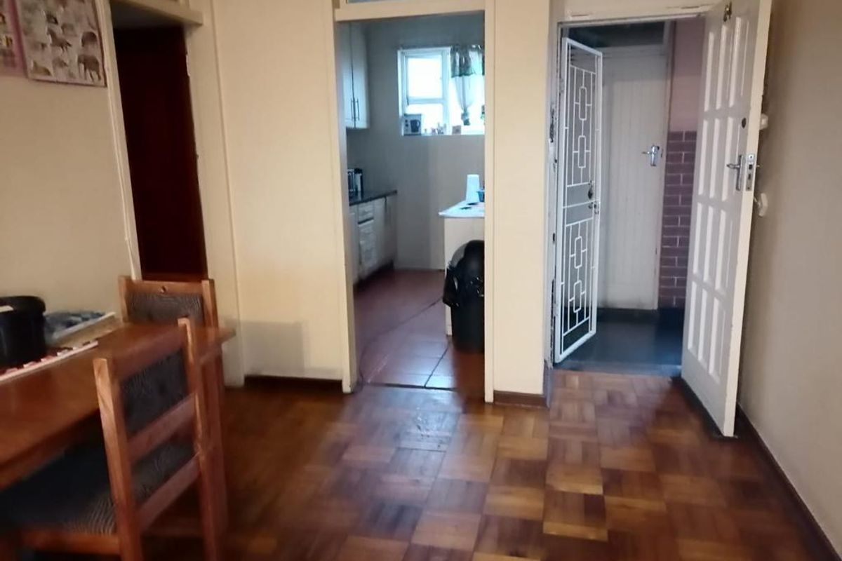 Living area featuring classic parquet flooring, leading through to a kitchen and an entrance with a security gate.