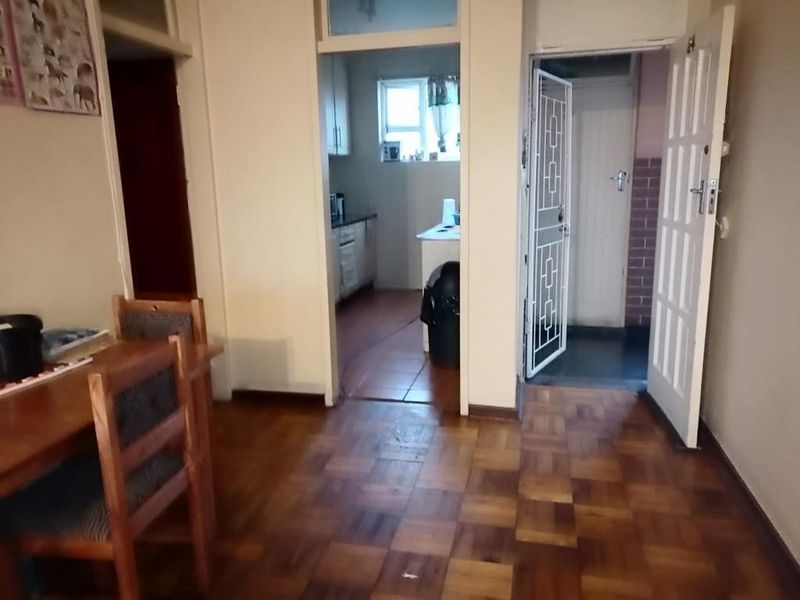 Living area featuring classic parquet flooring, leading through to a kitchen and an entrance with a security gate.