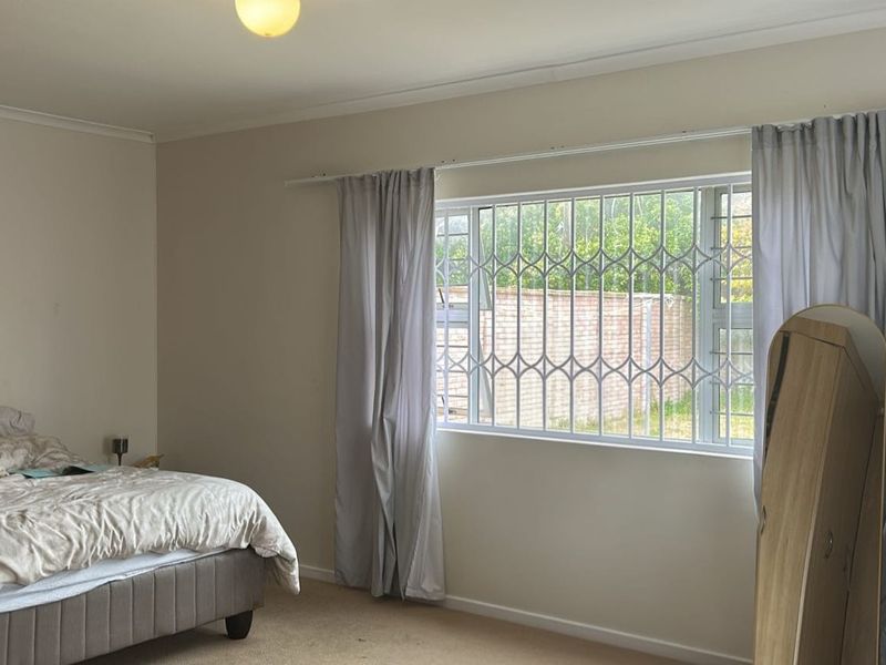 A spacious bedroom featuring neutral walls, carpeted flooring, and a window fitted with a security gate for added safety.