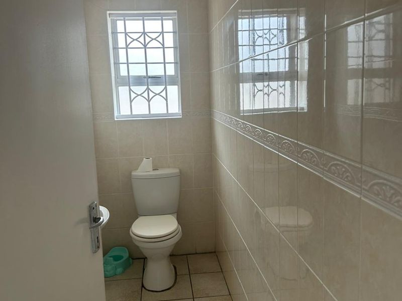 A compact bathroom featuring neutral ceramic wall and floor tiles, a standard toilet, and a window with security bars.