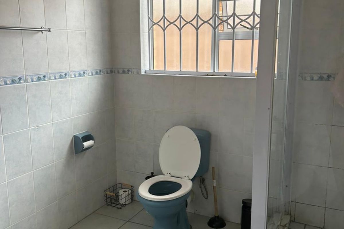 A functional bathroom featuring a shower enclosure, tiled walls and flooring, and a window with security bars.