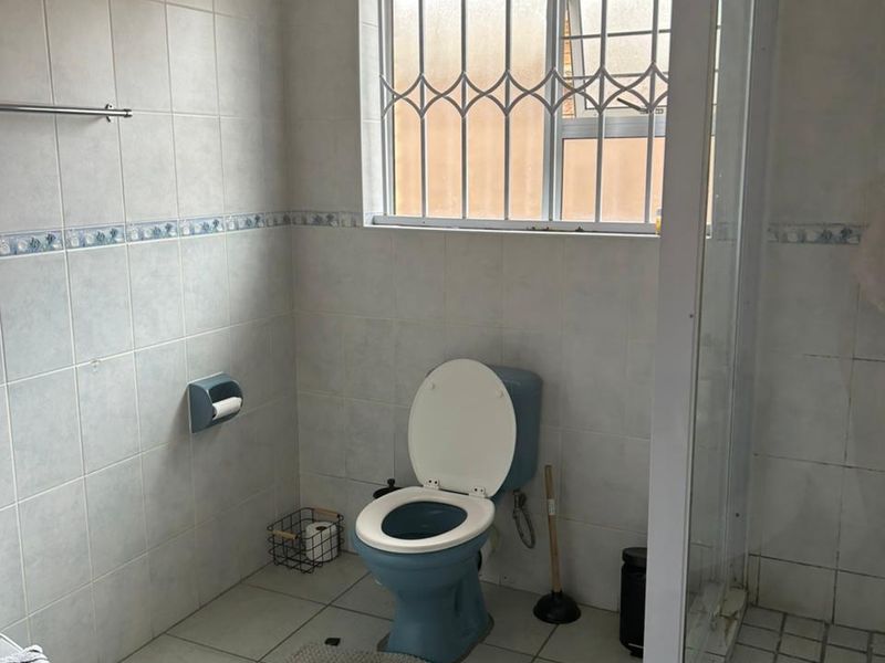 A functional bathroom featuring a shower enclosure, tiled walls and flooring, and a window with security bars.
