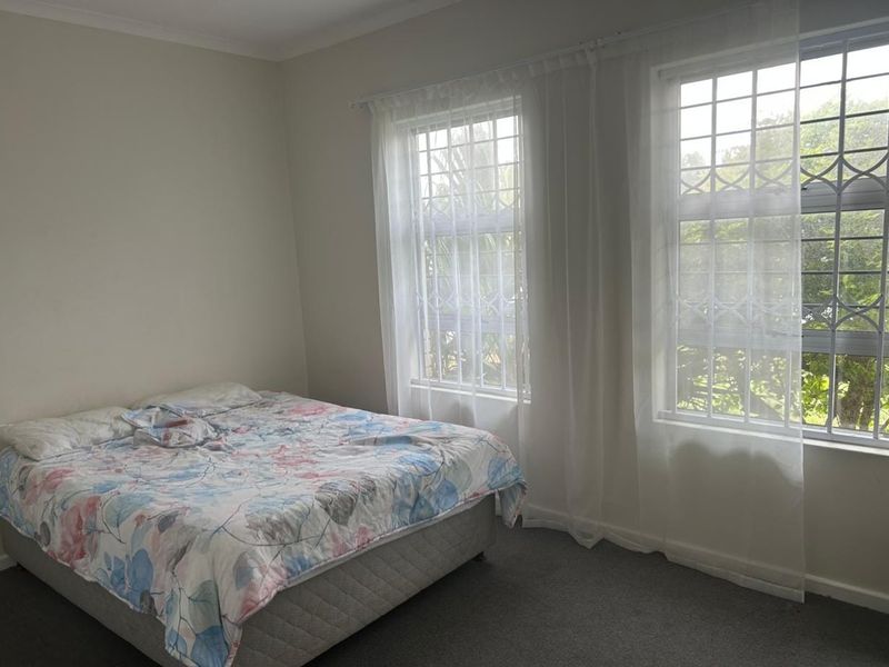 A bedroom featuring carpeted flooring and large windows fitted with security bars and curtain rails, offering natural light.