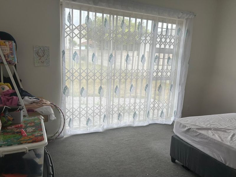 A bedroom featuring carpeted flooring and a large sliding glass door with an integrated security gate providing access to the exterior.