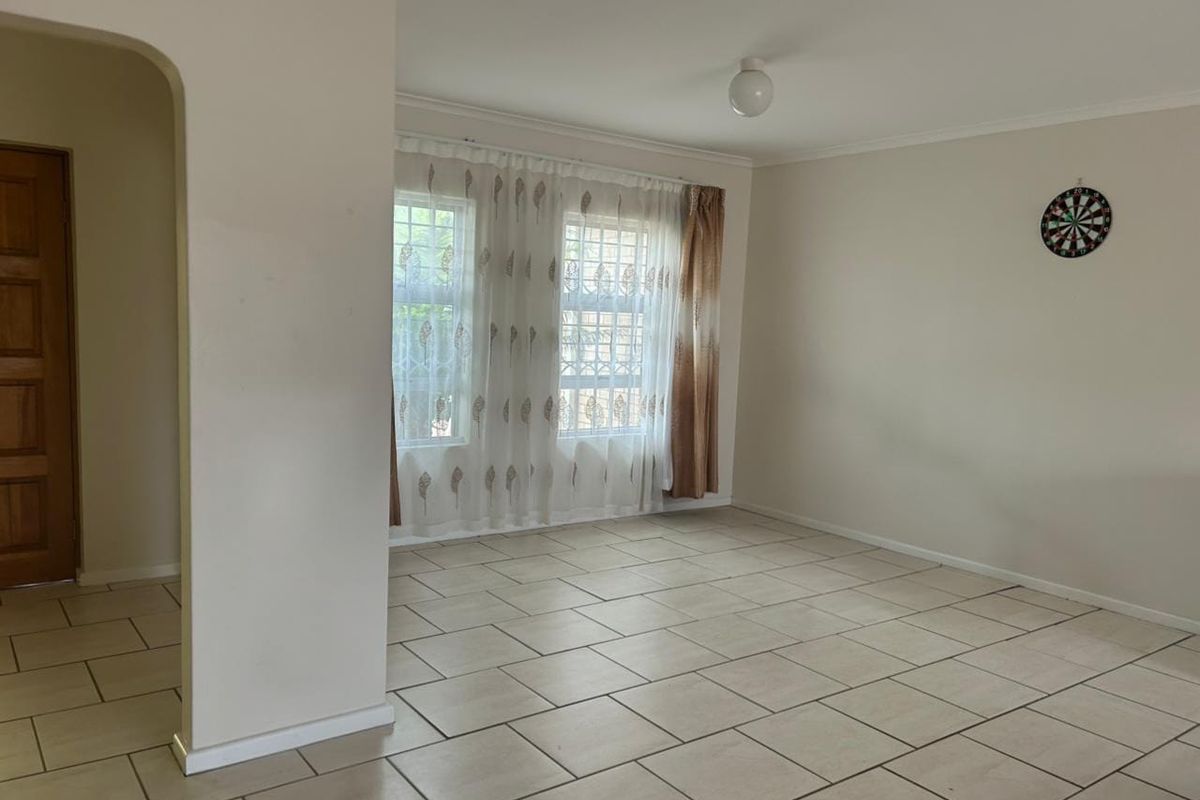 A spacious, empty living area featuring neutral tiled flooring, an arched entryway, and windows fitted with security bars.