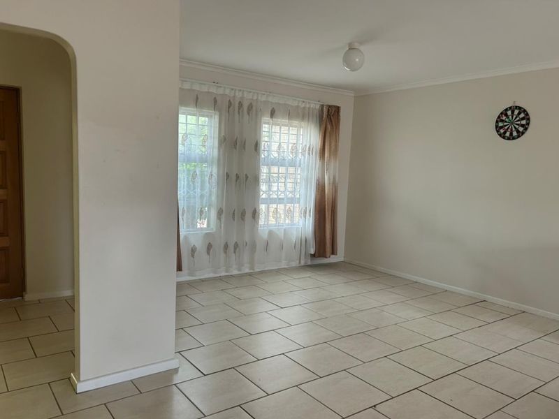 A spacious, empty living area featuring neutral tiled flooring, an arched entryway, and windows fitted with security bars.
