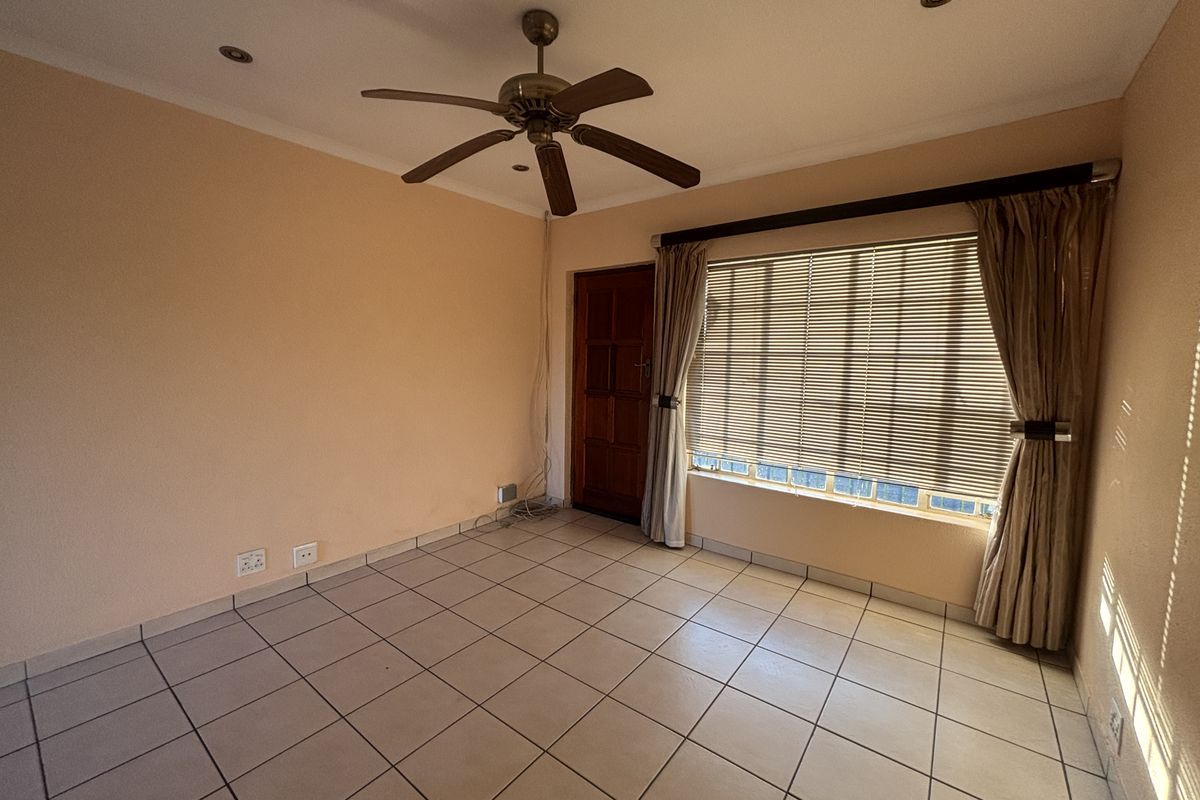 An empty living room featuring tiled flooring, a ceiling fan, recessed lighting, and large windows with fitted blinds and curtain rails.