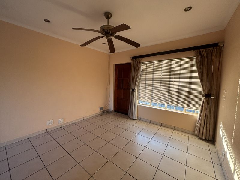 An empty living room featuring tiled flooring, a ceiling fan, recessed lighting, and large windows with fitted blinds and curtain rails.
