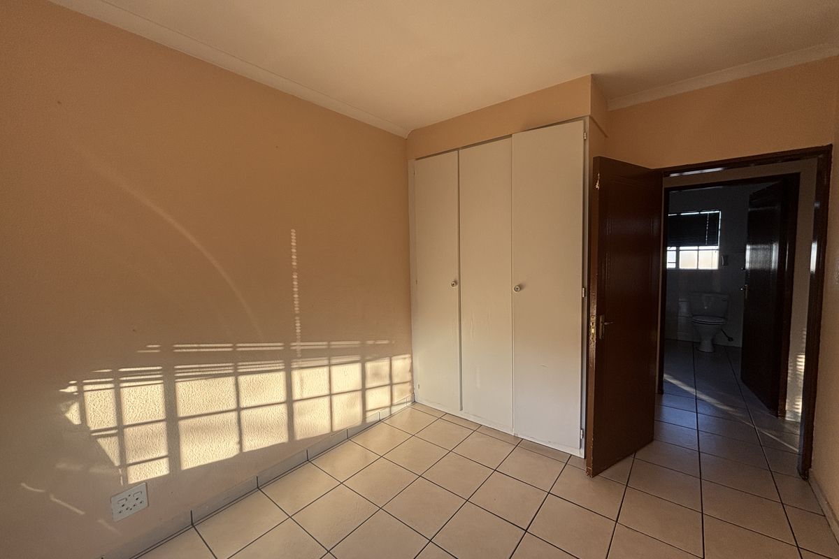 An empty bedroom featuring tiled flooring, built-in cupboards, and a doorway leading to an adjacent bathroom.