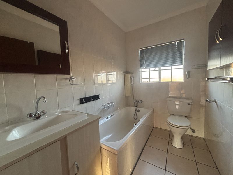 A functional bathroom featuring a bathtub, toilet, vanity basin, and tiled finishes, offering a clean and practical layout.