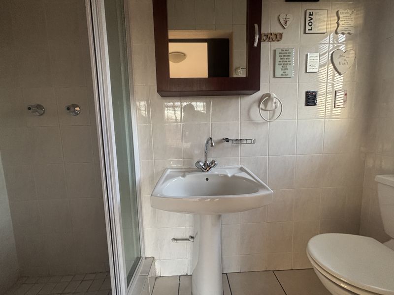 A functional bathroom featuring a pedestal basin, shower enclosure, and toilet with neutral wall tiling and a wall-mounted medicine cabinet.