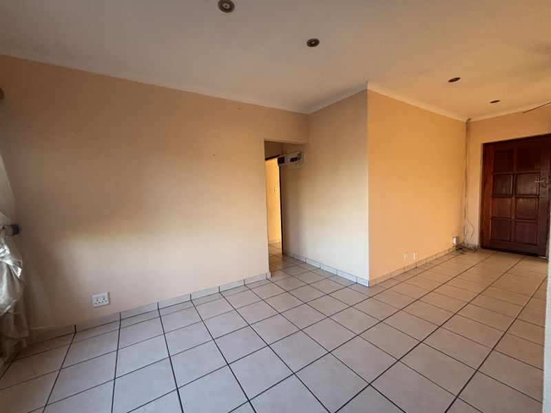 An empty living room featuring neutral tiled flooring, recessed downlights, and a solid wooden door, providing a blank canvas for interior design.
