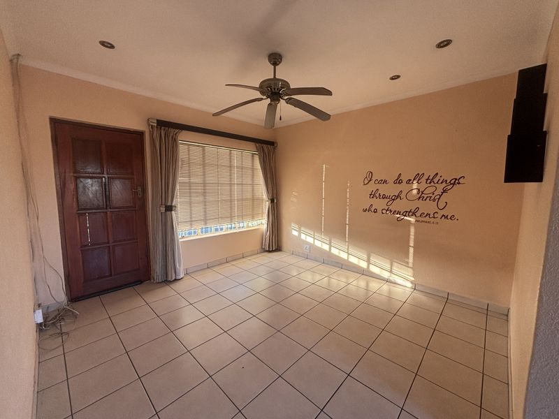 An empty living room featuring tiled flooring, a ceiling fan, recessed lighting, and a timber entrance door with venetian blinds.