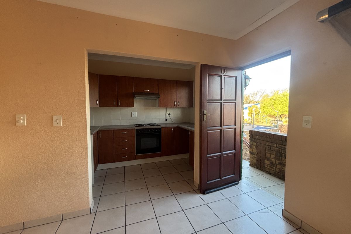 A functional kitchen featuring built-in wooden cabinetry, a hob, oven, and extractor fan, with tiled flooring and direct access to an outdoor area.