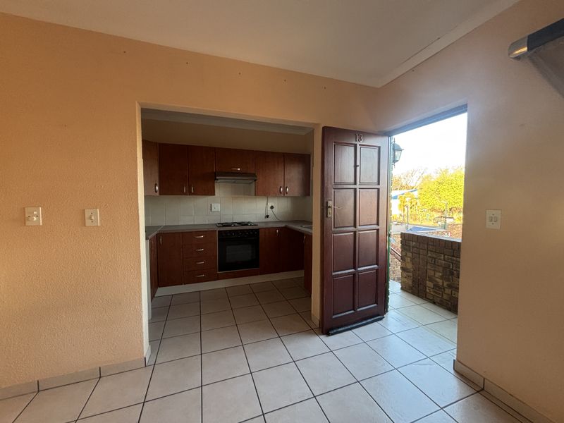 A functional kitchen featuring built-in wooden cabinetry, a hob, oven, and extractor fan, with tiled flooring and direct access to an outdoor area.