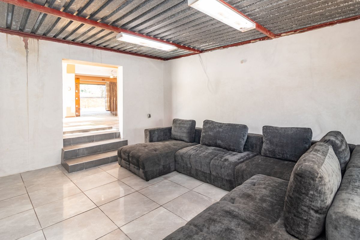 A living area featuring tiled floors and an exposed corrugated metal ceiling, leading to an adjacent space via a small set of stairs.
