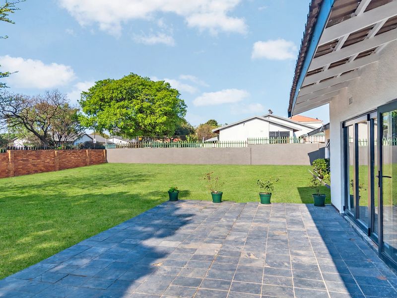A spacious rear garden featuring a tiled patio area and large folding glass doors providing seamless indoor-outdoor flow.